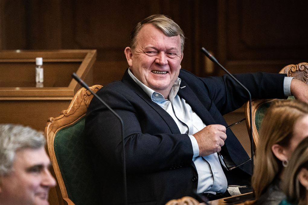 Lars Lække Rasmussen fotograferet i Folketingssalen med et kæmpe, snedigt smil. 