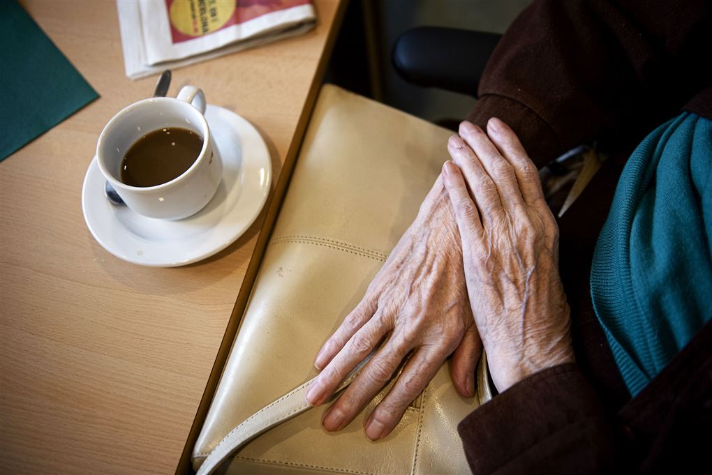 ældre person sidder ved bord med en kop kaffe