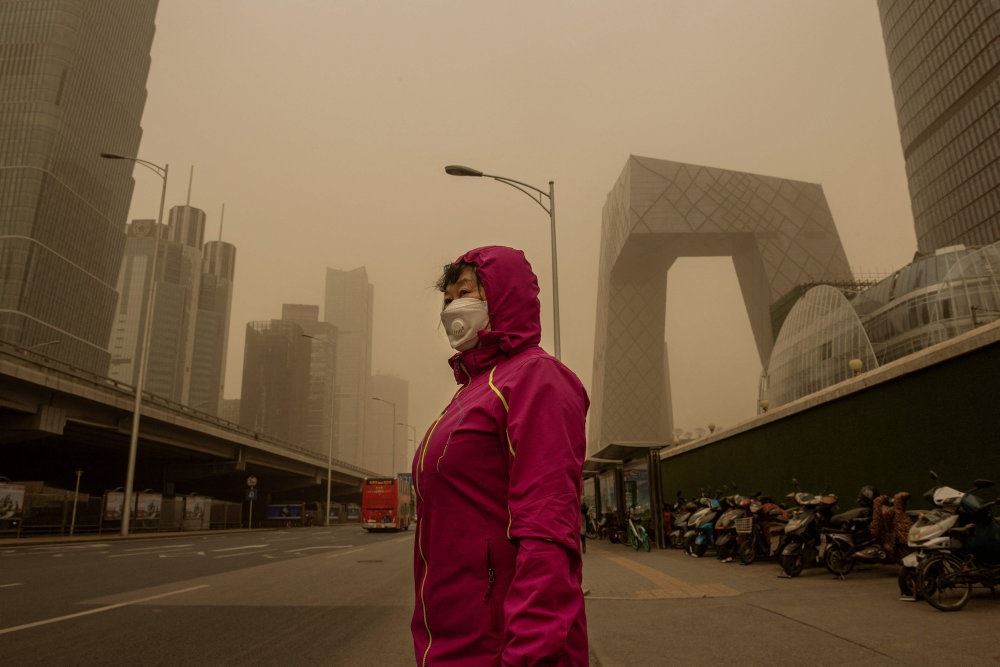 person i rødt tøj står i beijing under sandstorm