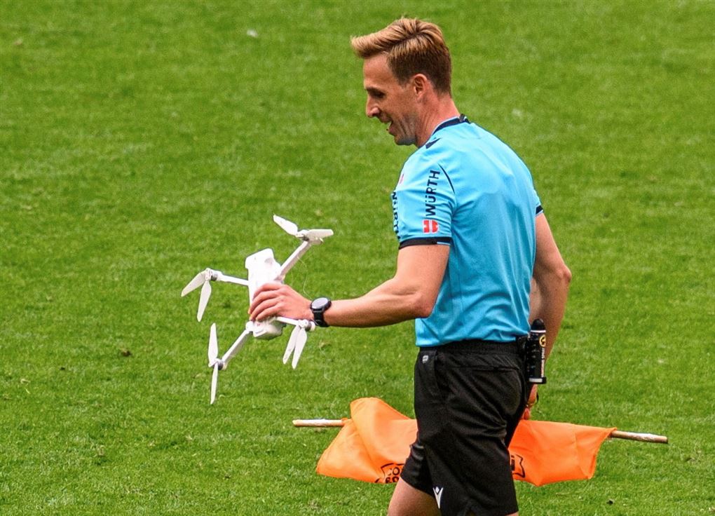 fodbolddommer går med drone og flag i hænderne