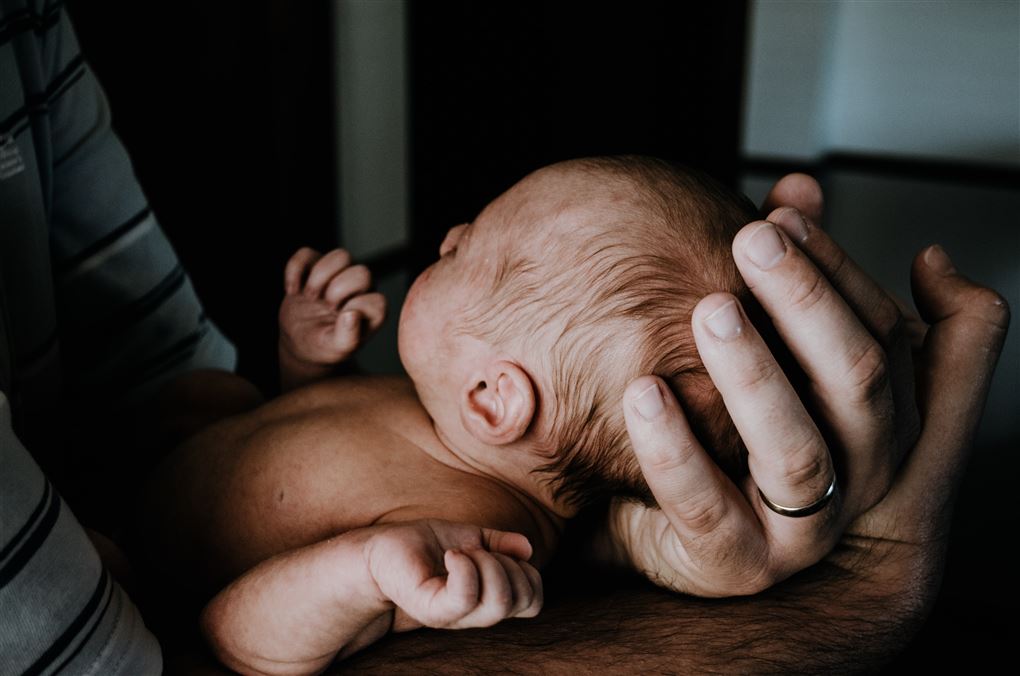 En nyfødt baby ligger i et par hænder.