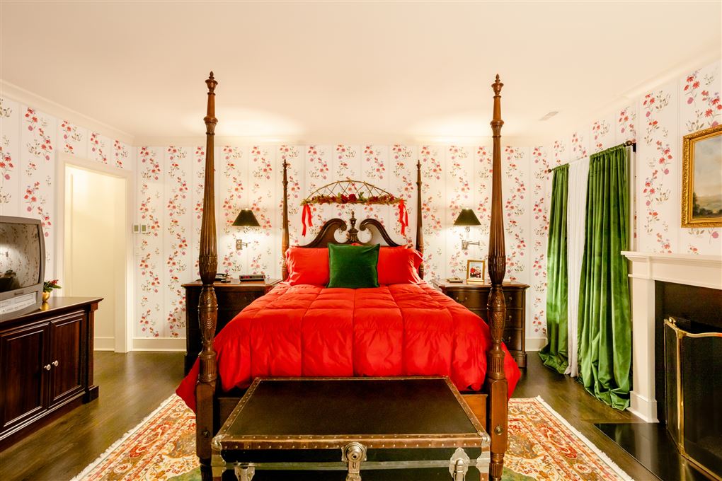 Soveværelset med et stor dobbeltseng med et meget rødt sengetæppe. Gardinerne er grønne og det hele virker meget julet.