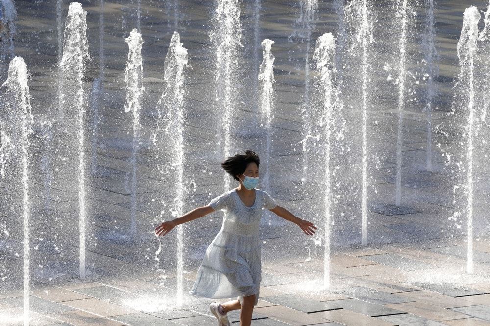 En pige med mundbind løber gennen springvand i Beijing i Kina
