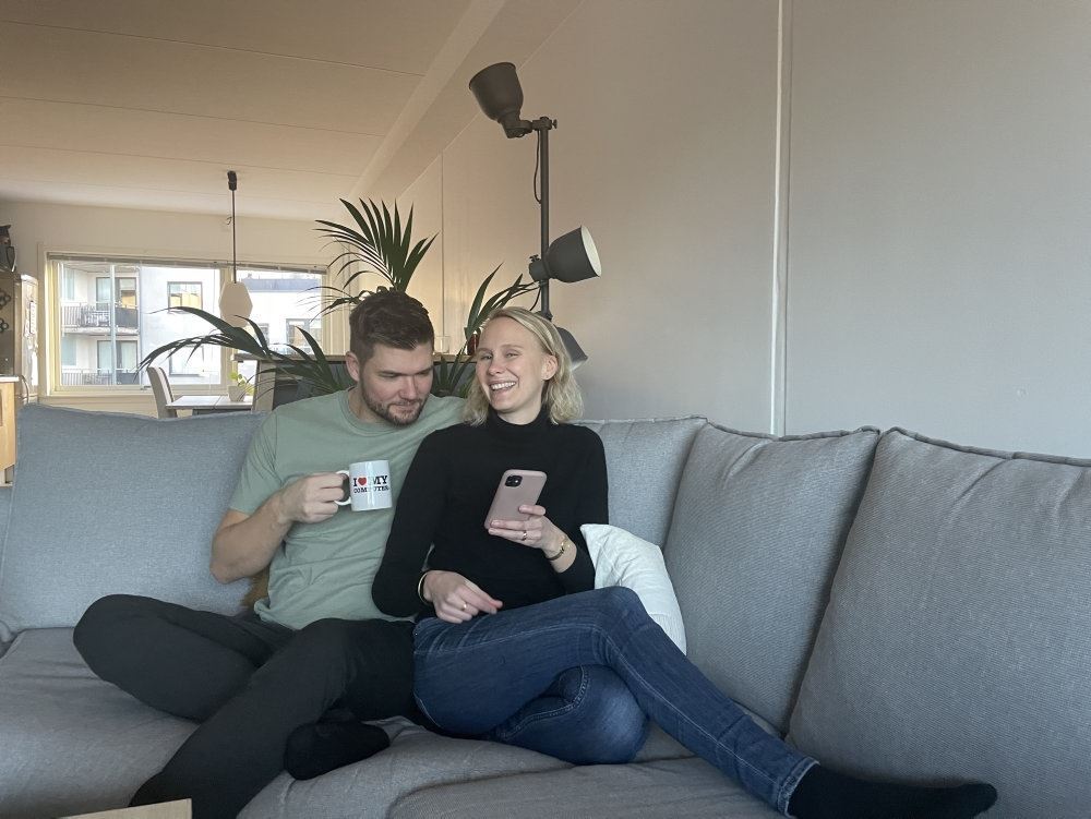 Parret sidder i en sofa med en kop kaffe og kigger ned i en telefon.