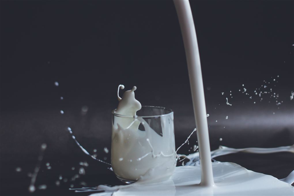 Mælk hældes ved siden af et glas