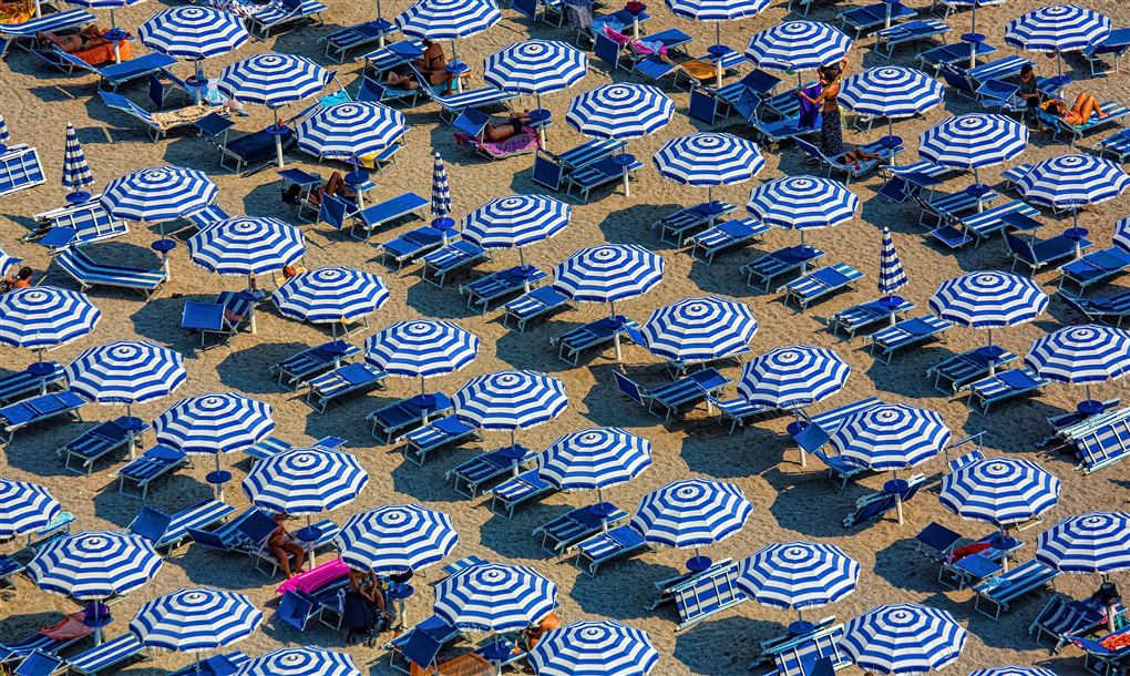 En strand fyld med blå og hvide parasoller