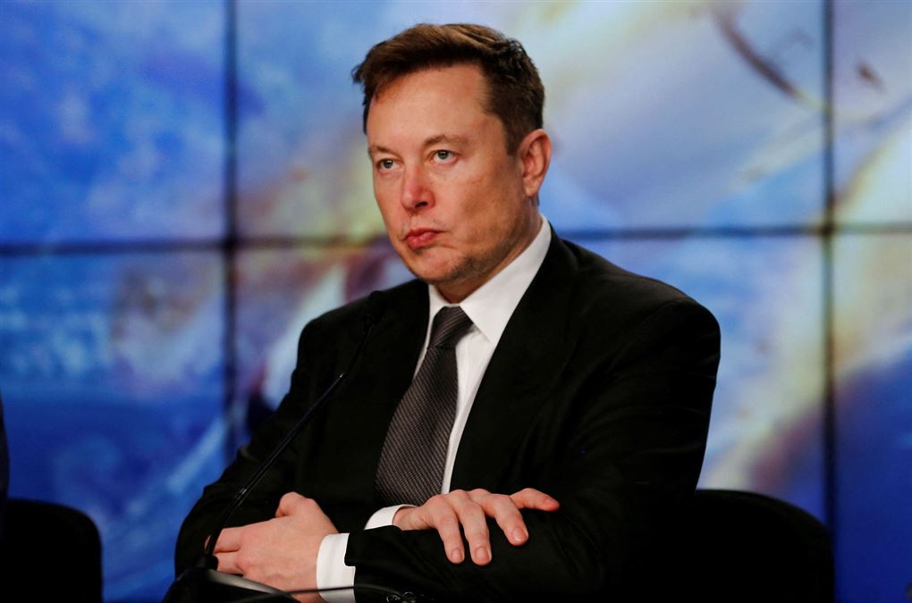 Elon Musk sidder med armene over kors og ser sur ud. 