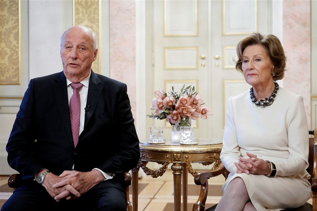Kong Harald og dronning Sonja sidder ved et guldbord og taler til pressen.