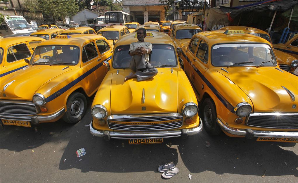 En indisk mand sidder oven på sin gule taxa