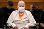 En mand klædt i hvidt med ansigtsmaske sidder i et retslokale