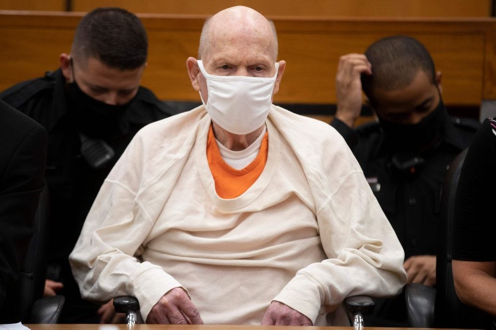 En mand klædt i hvidt med ansigtsmaske sidder i et retslokale