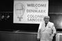 Billede af en ældre mand i hvid kittel og et skilt i baggrunden hvor der står Welcome Denmark
