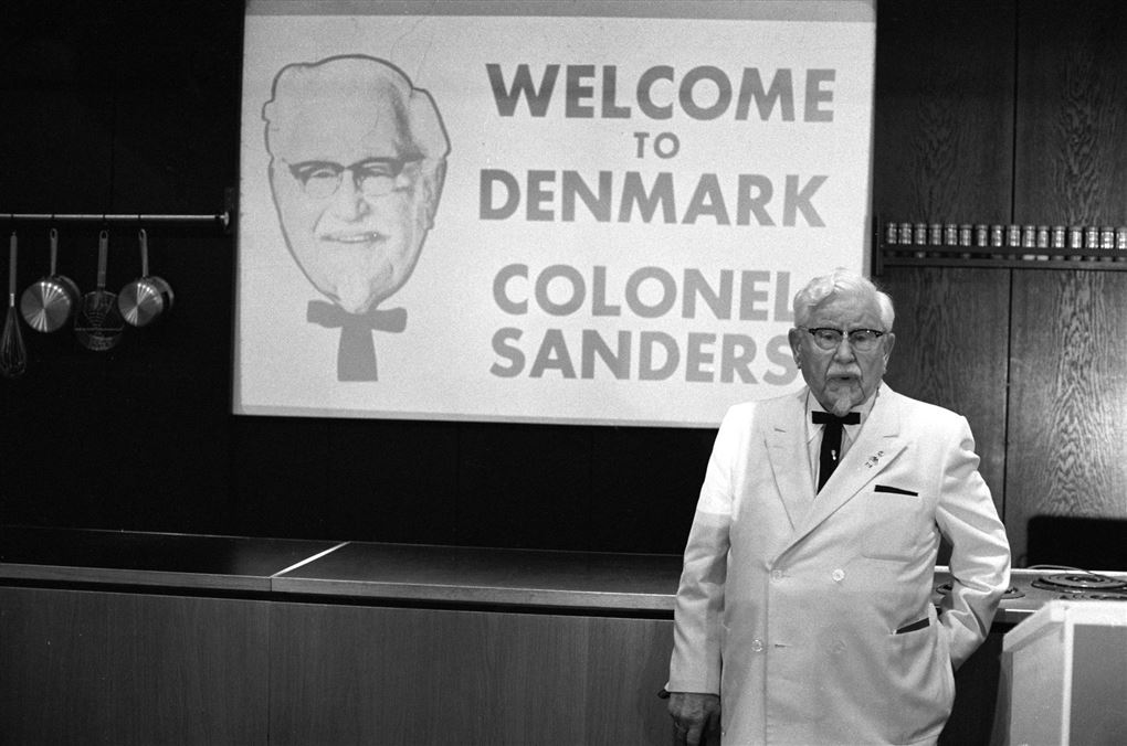 Billede af en ældre mand i hvid kittel og et skilt i baggrunden hvor der står Welcome Denmark