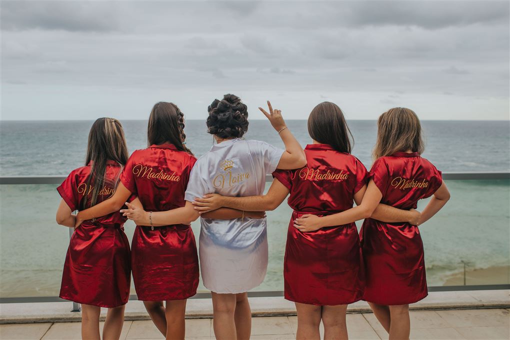 5 kvinder bagfra - fire af dem i røde silkekjoler - hende i midten har curlers og klædt i hvidt