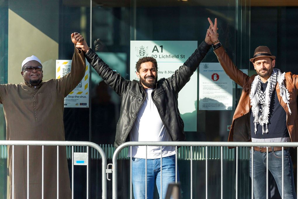 Tre mænd står med armene i vejret uden for retsbygning i New Zealand