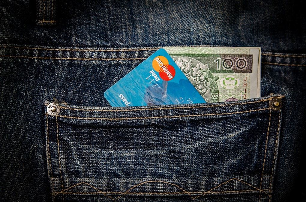 En jeans-baglomme, hvor der stikker et kreditkort samt nogle dollars op fra