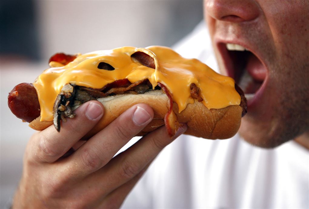 Mand æder en hotdog med ameltet ost henover