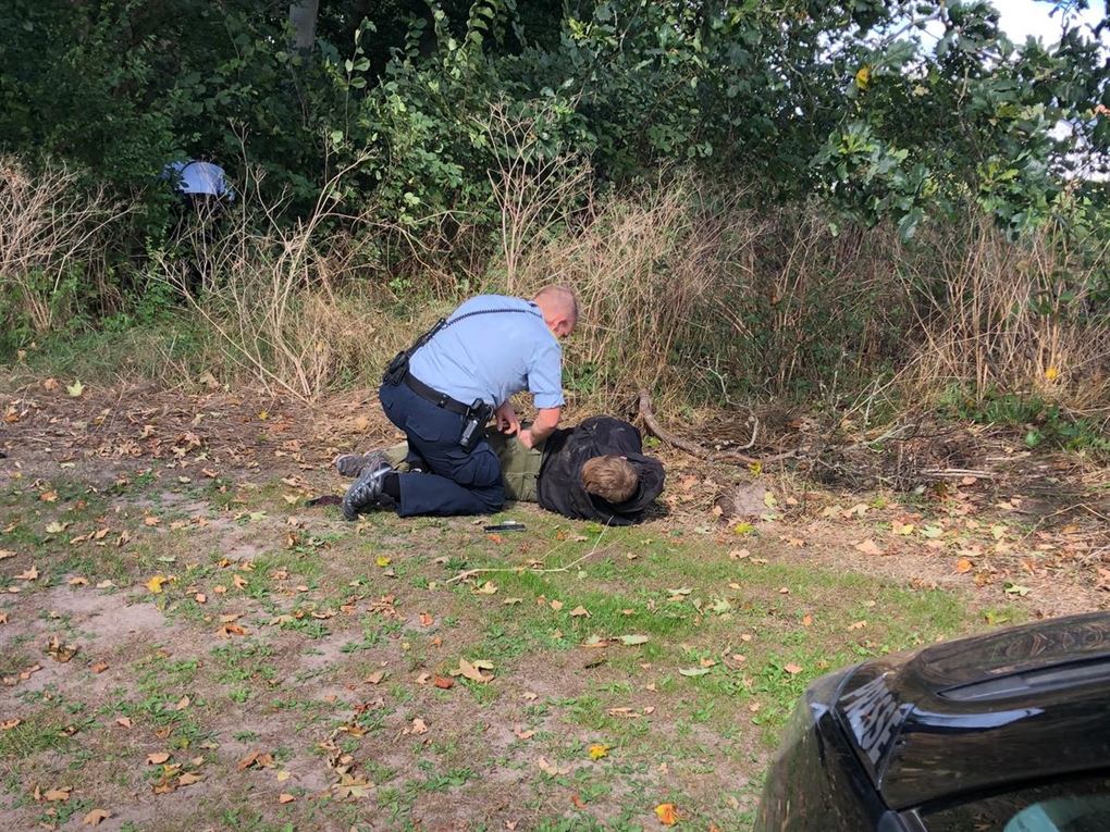 Ung mand i mørk trøje ligger på jorden, mens en betjent knæler ned og lægger ham i håndjern