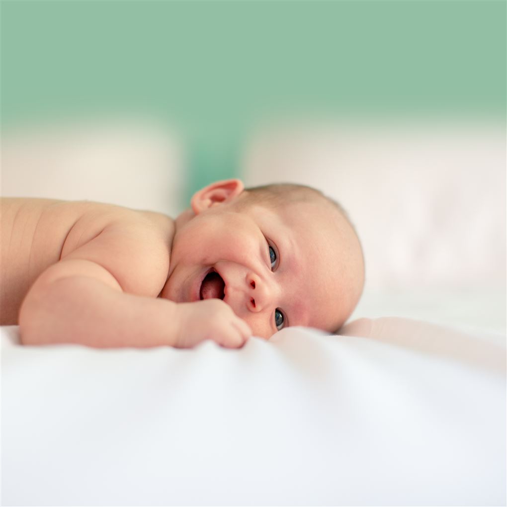 En frinende baby på et blødt underlag med en grøn væg i baggrunden