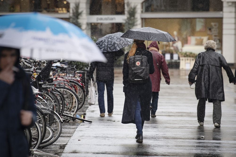 Folk med paraplyer og vintertøj går med ryggen til ned af en gade.