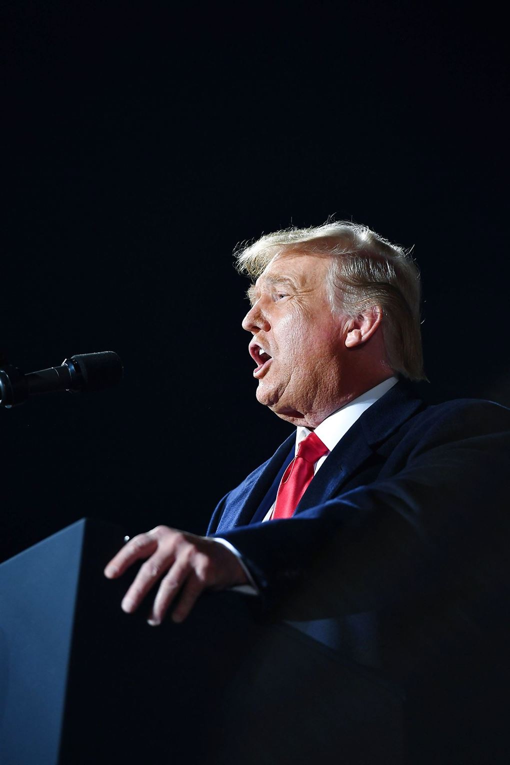 Nærbillede af Donald Trump på en talerstol med et rødt slips og åben mund. Den amerikanske præsident ses i profil. 