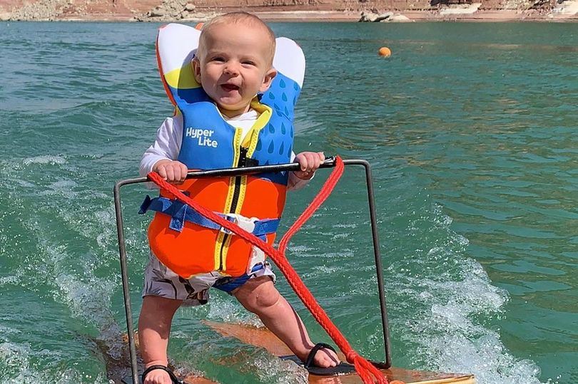 Seks måneder gammel dreng smiler mens han står på vandski 