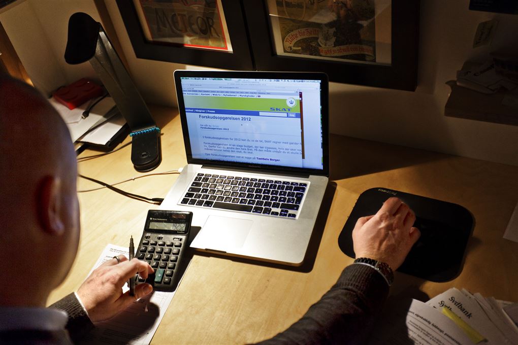 En mand sidder ved en computer med musen i den ene hånd og en lommeregner i den anden. Han ses fra ryggen. 