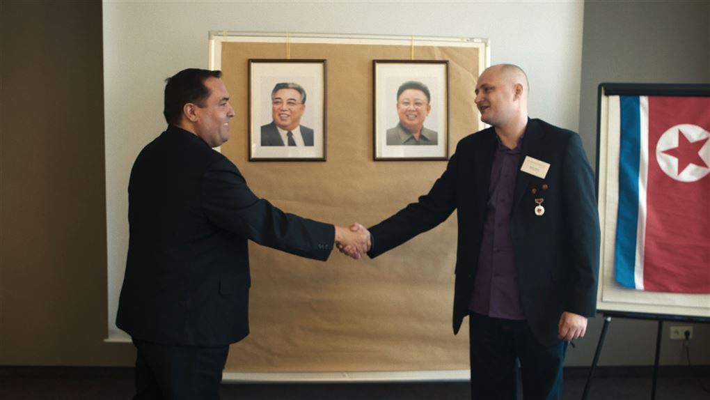 To mænd giver hånd foran billederne af nordkoreanske diktarorer 