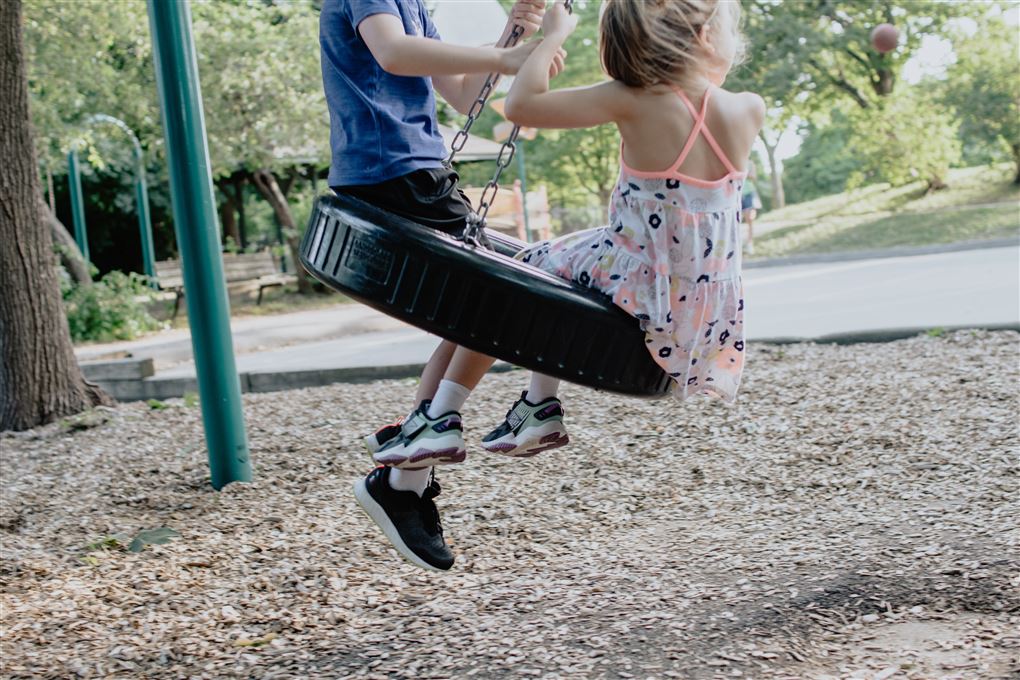 En lille pige og en dreng gynger på en legeplads. Man ser kun deres fødder og overkroppe. 