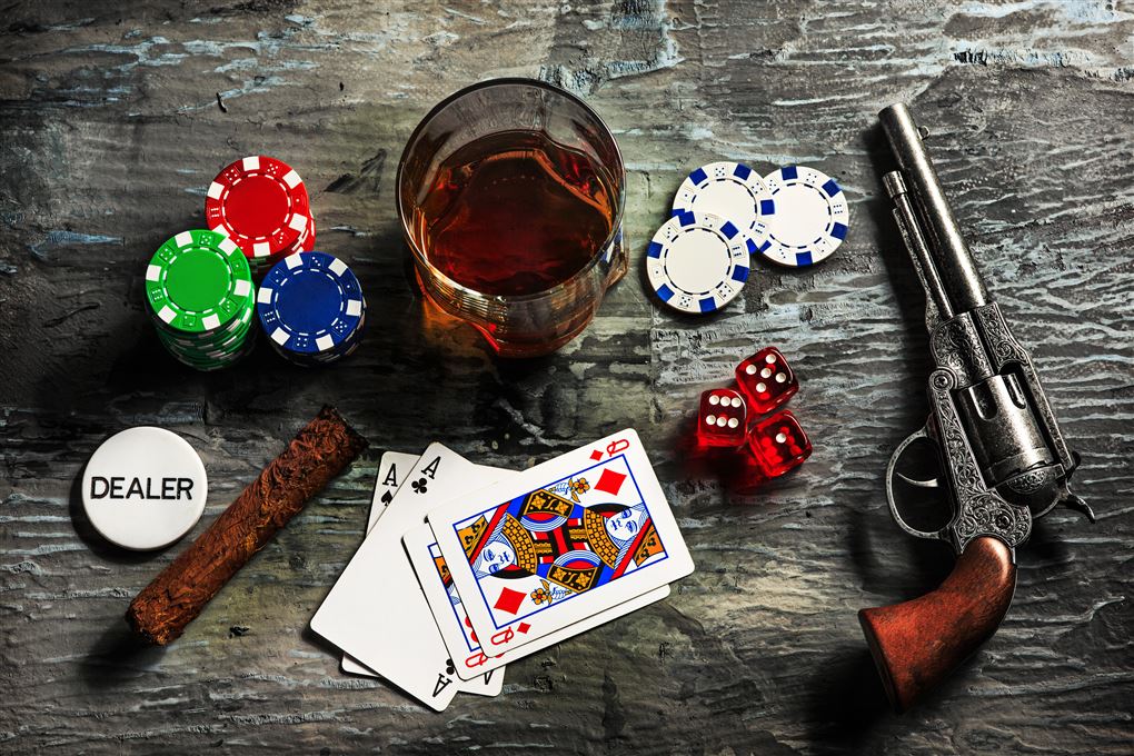 Jetoner, kort, terninger, en cigar, en whisky og en Colt revolver på et bord