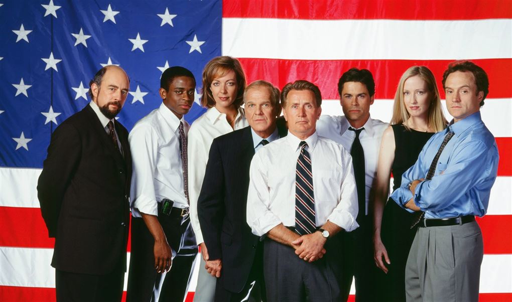 De medvirkende i West Wing med Martin Sheen i midten foran et amerikansk flag