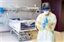 sygeplejerske med visir og mundbind foran tom hospitalsseng 