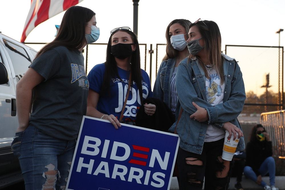 fire kvinder med ansigtsmaske står med skilt med navnene Biden Harris