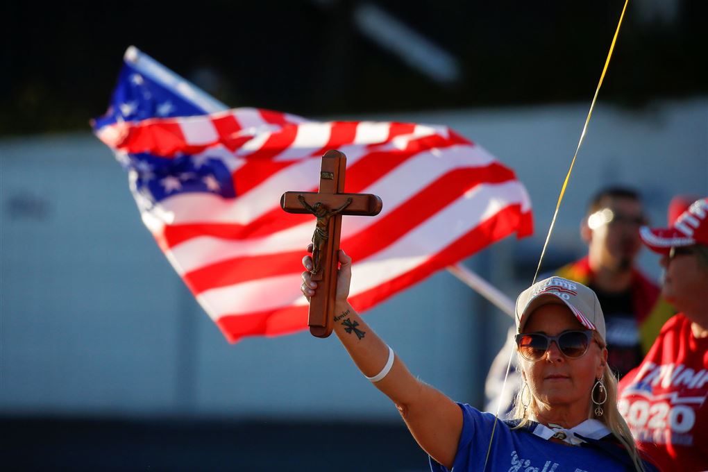 kvinde med krucifiks i strakt arm med det amerikanske flag i baggrunden