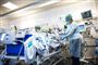 To sygeplejersker iført alverdens værnemidler tager sig af en patient på en hospitalsstue.