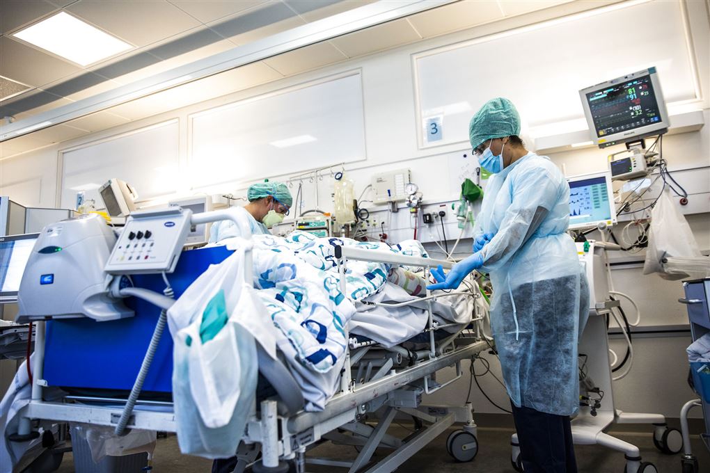 To sygeplejersker iført alverdens værnemidler tager sig af en patient på en hospitalsstue.