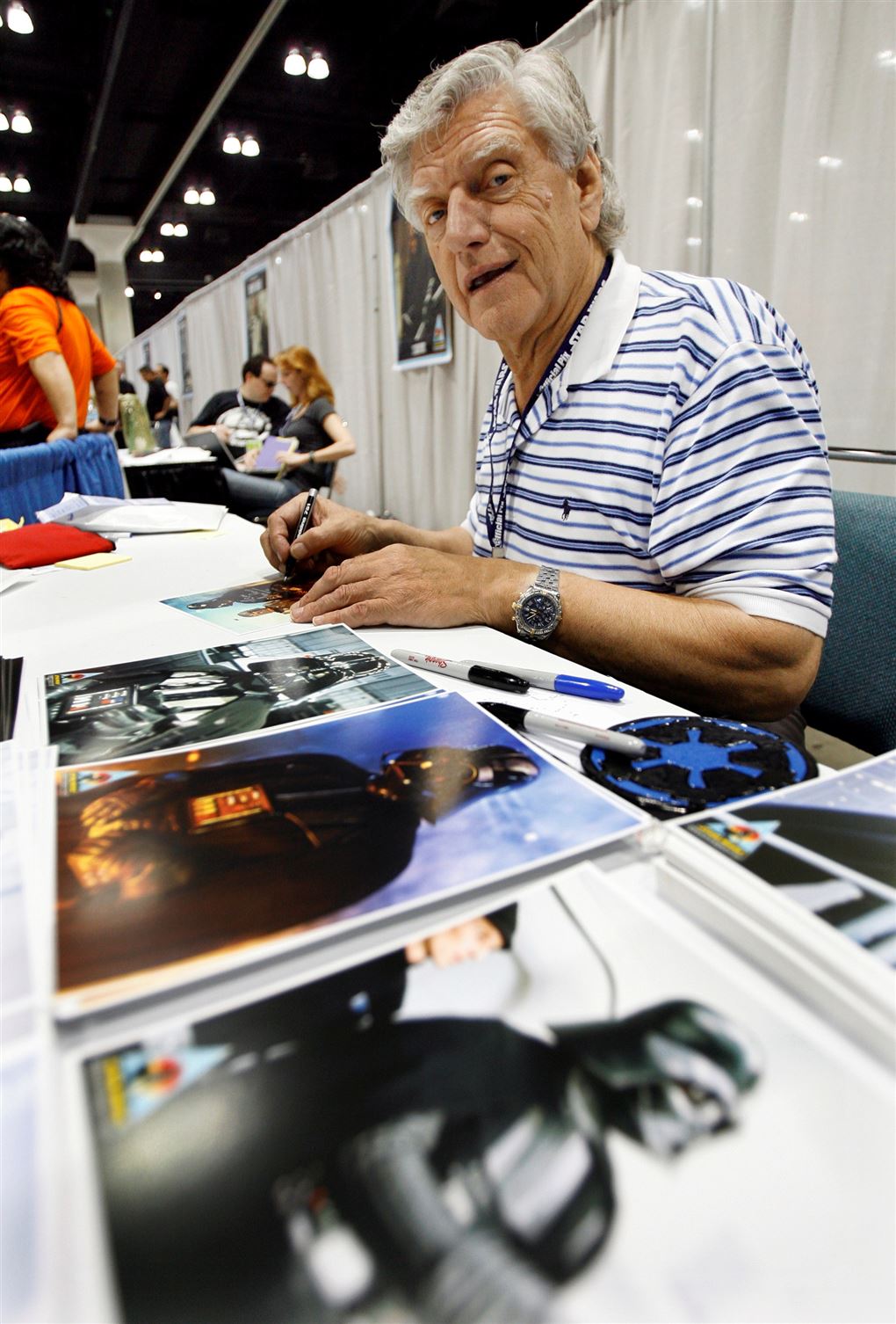 En gråhåret mand i stribet t-shirt signerer billeder
