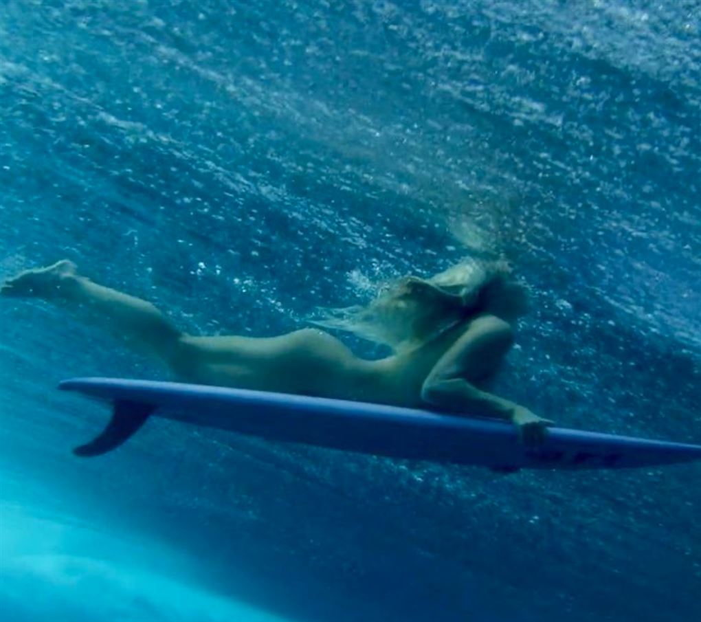 En nøgen kvinde under vand på surfbræt