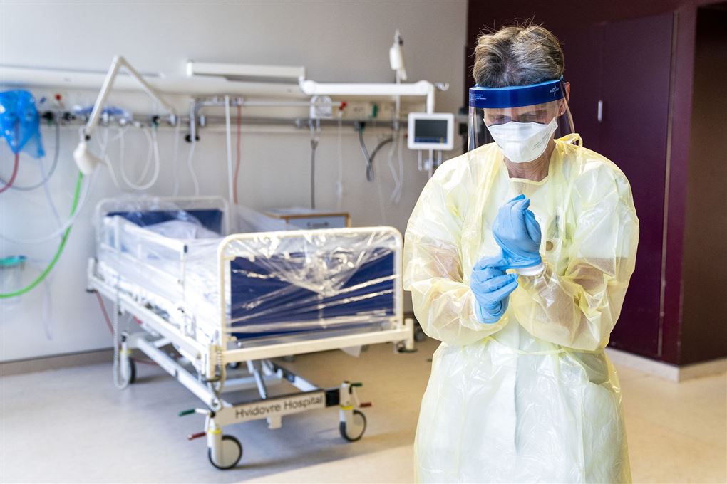 sygeplejerske med handsker og maske står foran tom hospitalsseng