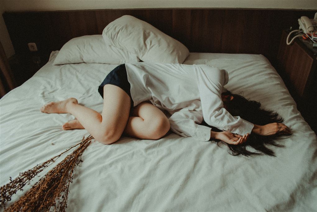 kvinde ligger på seng med hænderne for hovedet