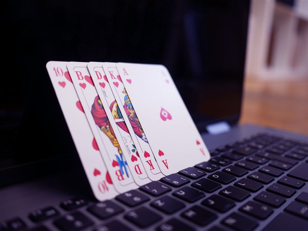 Fem spillekort, der læner sig op af en åben pc