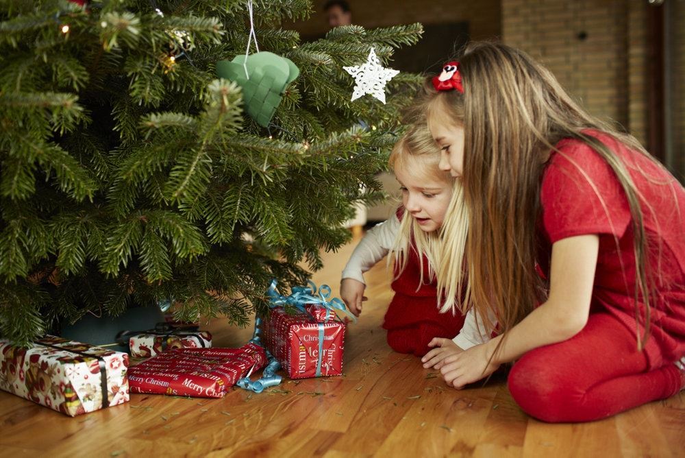 to børn sidder og kigger på gaver under træet