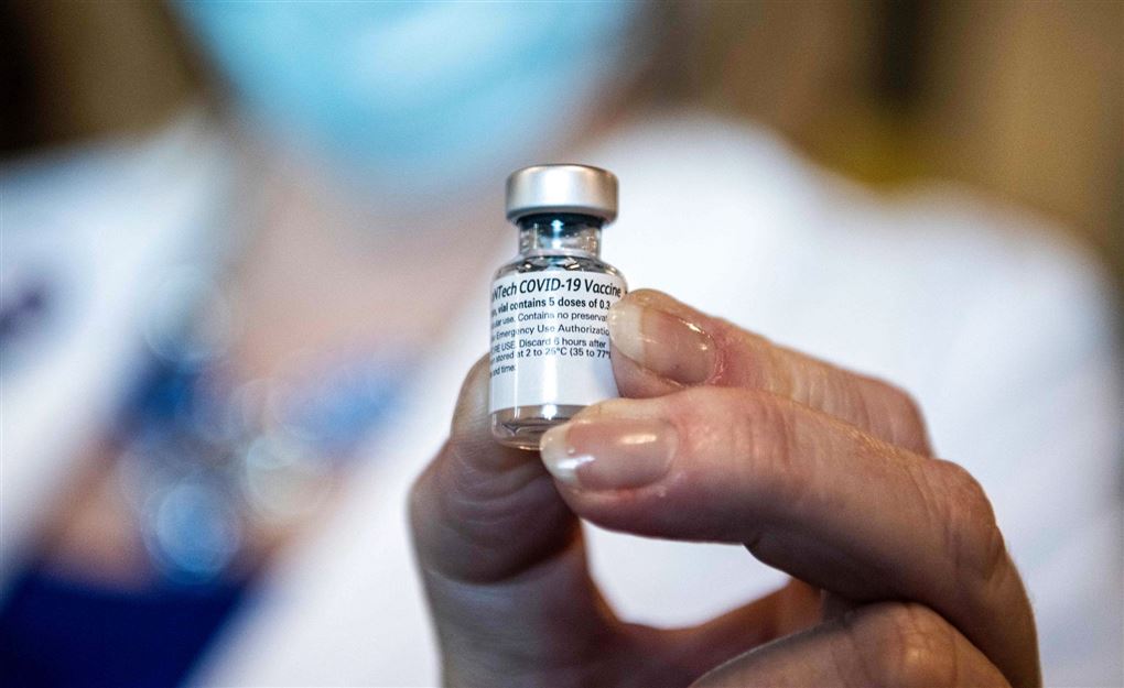 person står med en flaske vaccine i hånden