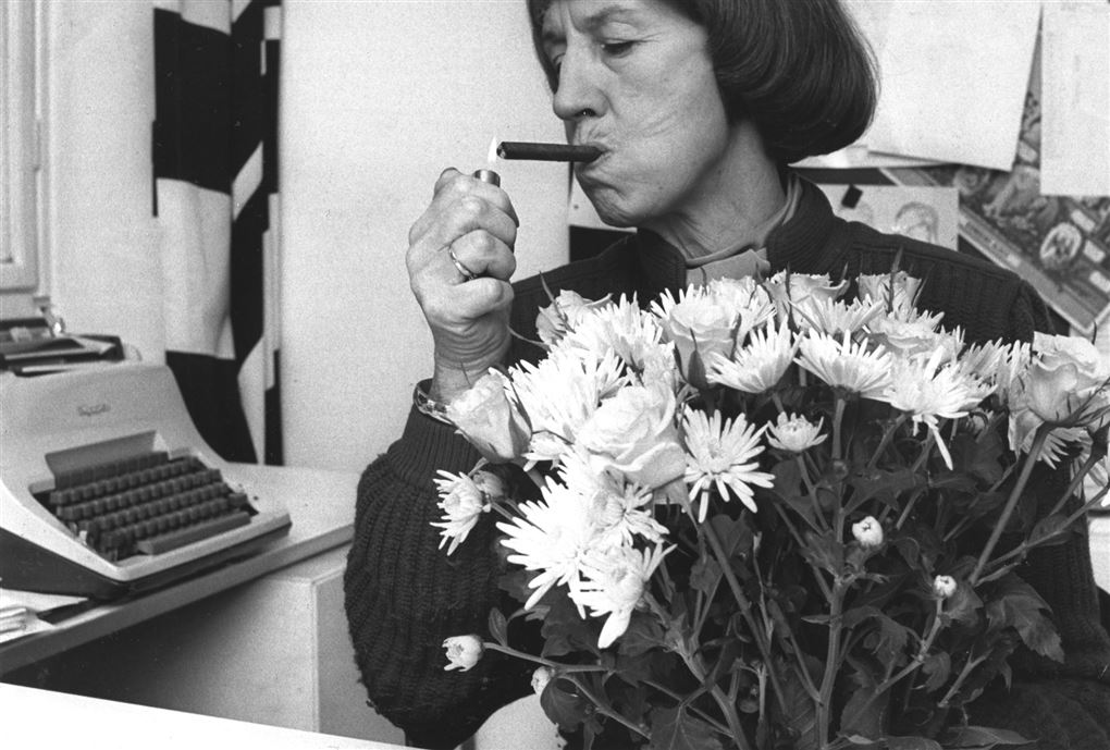 Lise Nørgaard er ved at tænde en cerut med en lighter i den anden hånd har hun en enorm buket blomster.