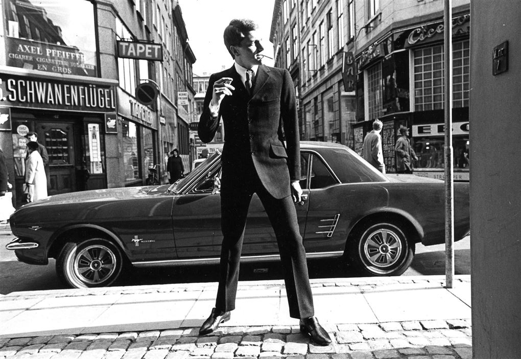 En ung mand i jakkesæt med en Ford Mustang i baggrunden i en gade i København