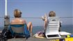 To kvinder med ryggen til sidder i klapstole og kigger ud over havet.