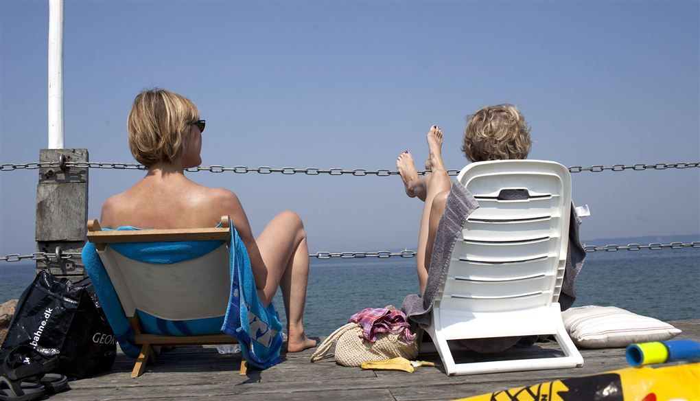 To kvinder med ryggen til sidder i klapstole og kigger ud over havet.