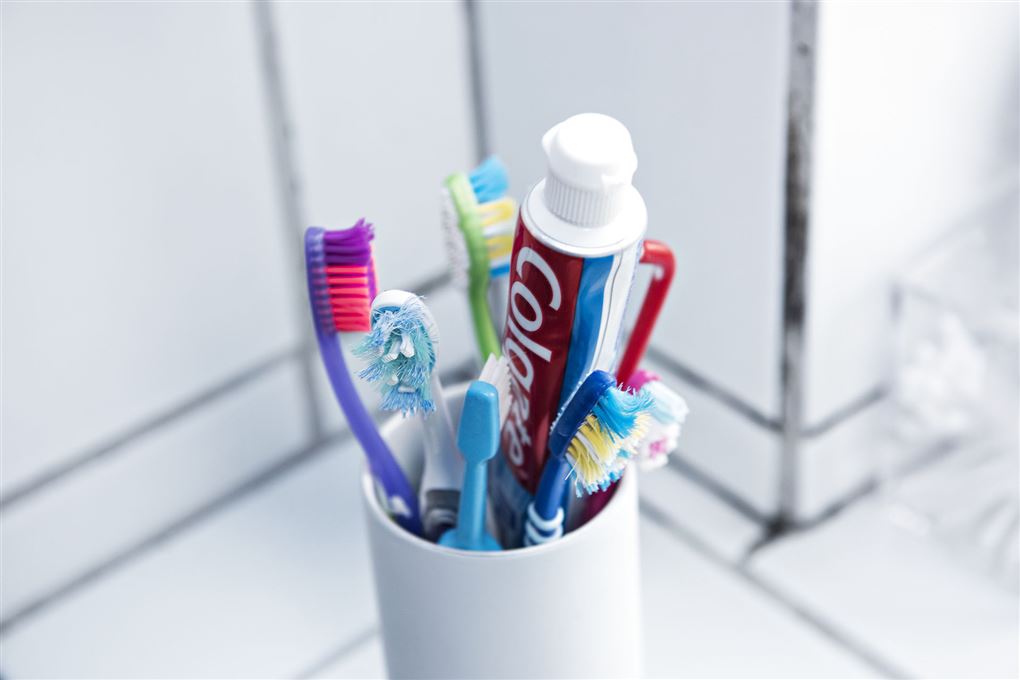 Et glas med forskellige tandbørster og en tube tandpasta.