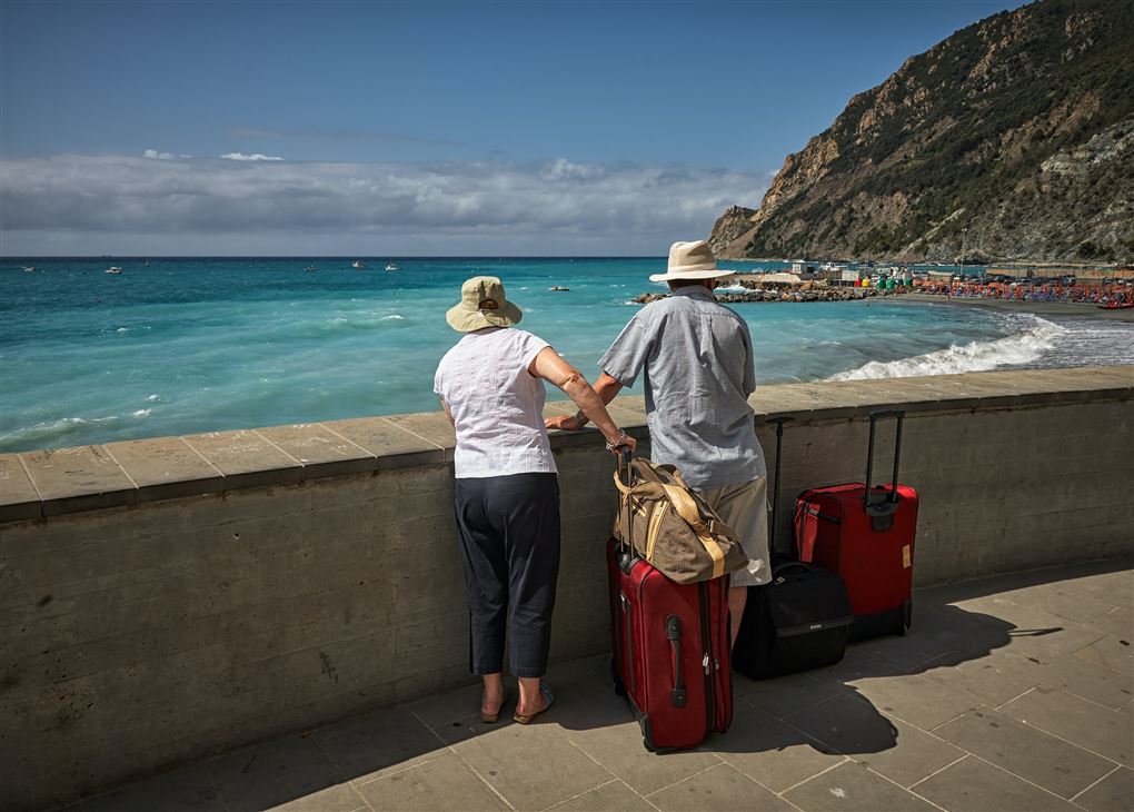 Et ældre par med kufferter kigger ud over en strand