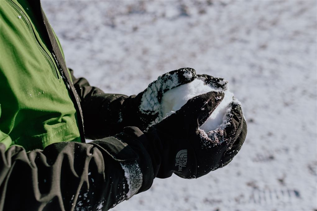 person med handsker former snebold i hænderne